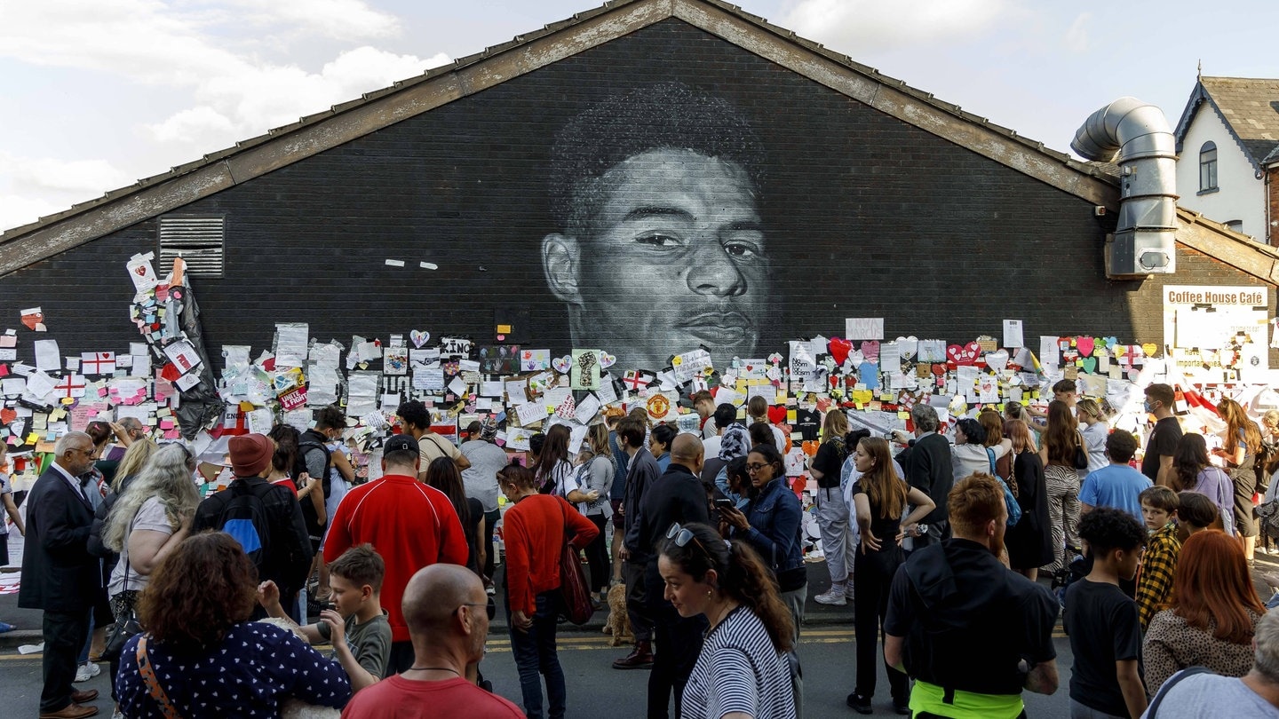 Menschen stehen vor einem Portrait des englischen Nationalspielers Marcus Rashford. Nachdem dieser einen Elfmeter im Finale der Europameisterschaft gegen Italien verschossen hatte, gab es zahlreiche rassistische Anfeindungen. (Foto: IMAGO, xDanielxChesterton/phcimages.com/CoverxImage)