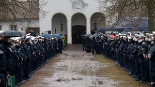 Polizisten und Polizistinnen stehen an der Kirche Spalier beim Gedenkgottesdienst für eine getötete Polizistin. Nach der Bestattung eines ermordeten Polizisten wird nun auch seine getötete Kollegin beigesetzt. Der 29 Jahre alte Polizeikommissar und die 24 Jahre alte Polizeianwärterin waren am 31. Januar während einer Fahrzeugkontrolle bei Kusel erschossen. (Foto: dpa Bildfunk, picture alliance/dpa | Harald Tittel) Polizisten und Polizistinnen stehen an der Kirche Spalier beim Gedenkgottesdienst für eine getötete Polizistin. Nach der Bestattung eines ermordeten Polizisten wird nun auch seine getötete Kollegin beigesetzt. Der 29 Jahre alte Polizeikommissar und die 24 Jahre alte Polizeianwärterin waren am 31. Januar während einer Fahrzeugkontrolle bei Kusel erschossen.