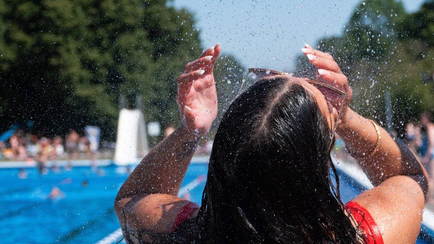 Eine junge Frau kühlt sich bei hochsommerlichen Temperaturen unter der Dusche von einem Schwimmbad ab.