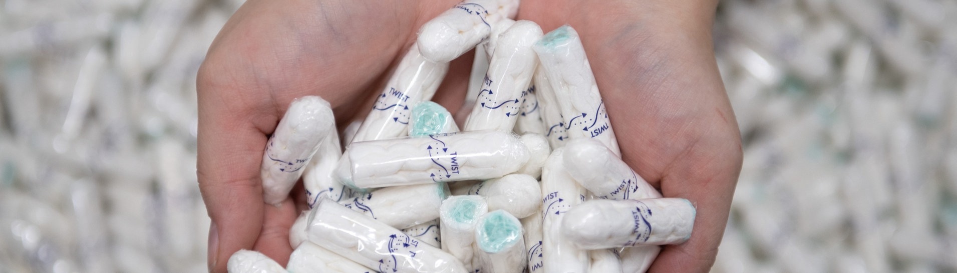 Eine Produktionsarbeiterin hält viele Tampons in den Händen und zeigt sie in die Kamera. (Foto: dpa Bildfunk, picture alliance/dpa/dpa-Zentralbild | Sebastian Kahnert)