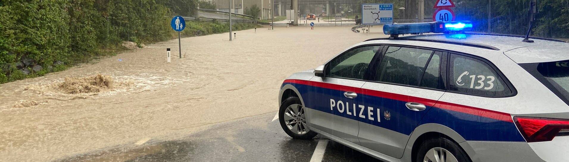 Ein Polizeifahrzeug steht nach Starkregen an einer überschwemmten Straße bei Wolfurt in der Nähe von Bregenz, Vorarlberg, Österreich. (Foto: dpa Bildfunk, picture alliance/dpa | Davor Knappmeyer)