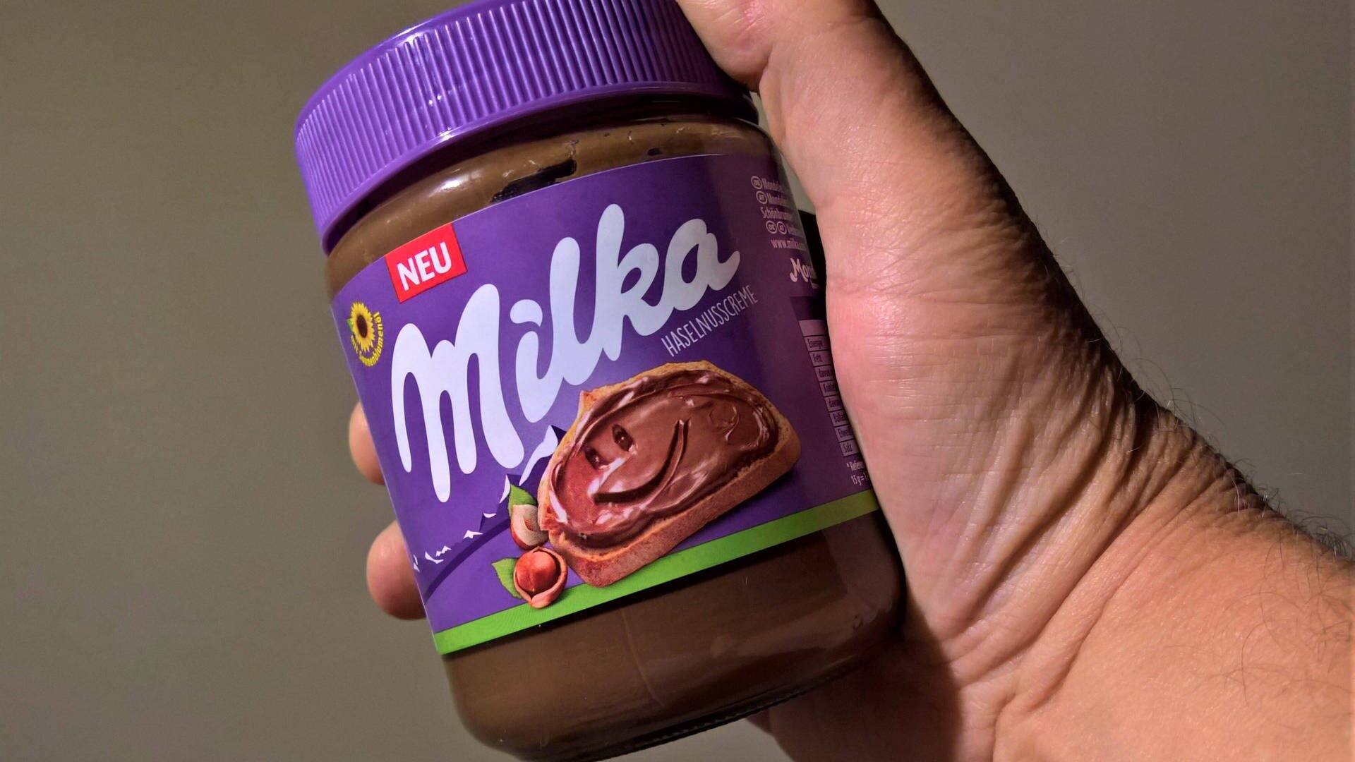 Milka Haselnusscreme, Schokoladen - Brotaufstrich, eine Hand hält ein Glas davon in die Kamera. (Foto: IMAGO, IMAGO / Manfred Segerer)