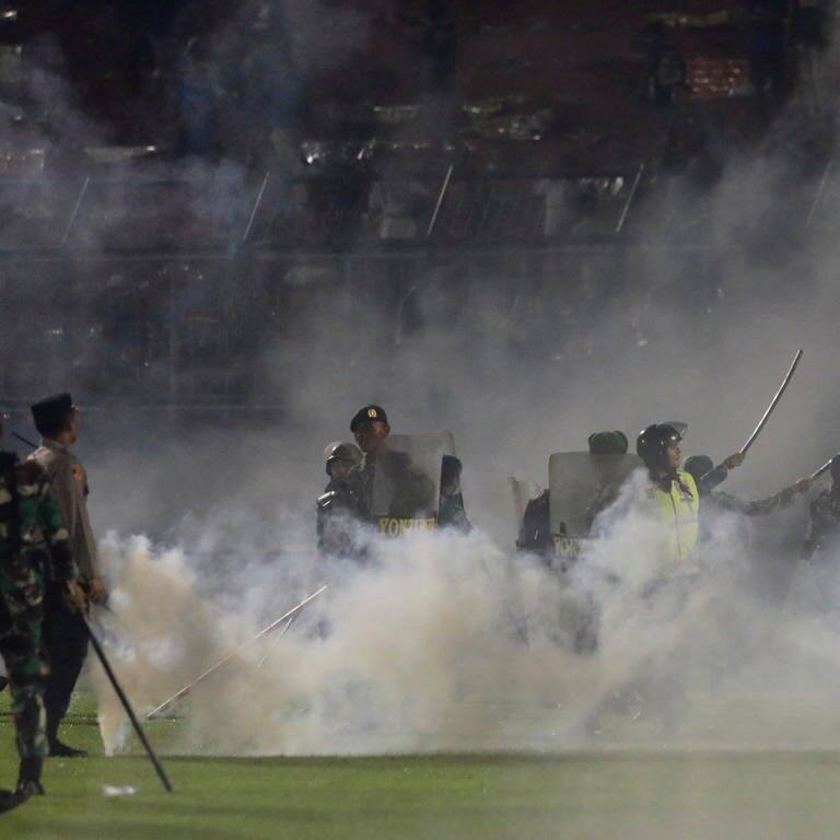 Polizisten und Soldaten stehen inmitten von Tränengasrauch bei einem Erstliga-Spiel zwischen Arema FC und Persebaya FC.  (Foto: dpa Bildfunk, picture alliance/dpa/AP | Yudha Prabowo)