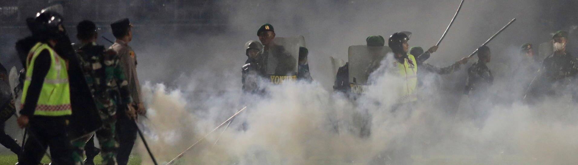Polizisten und Soldaten stehen inmitten von Tränengasrauch bei einem Erstliga-Spiel zwischen Arema FC und Persebaya FC.  (Foto: dpa Bildfunk, picture alliance/dpa/AP | Yudha Prabowo)