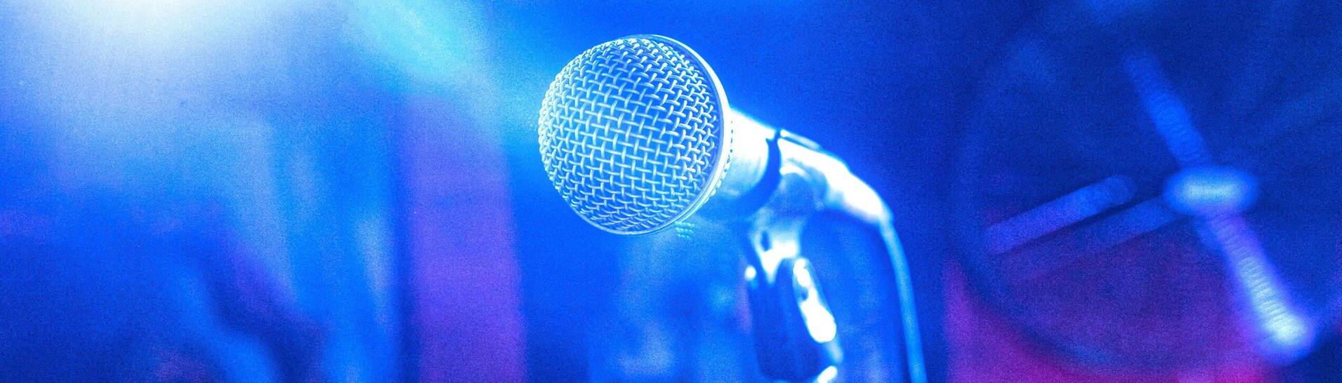 Ein blau beleuchtetes Mikrophon auf einem Ständer (Foto: IMAGO, IMAGO/YAY Images)