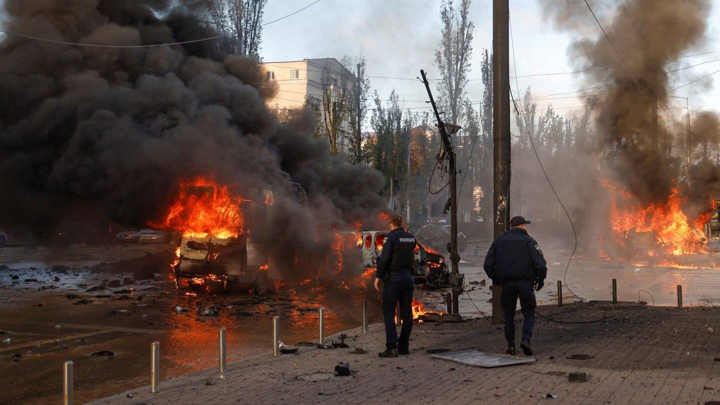 Zwei Polizisten stehen an einer Kreuzung in Kiew, auf der Autos brennen. (Foto: Reuters, REUTERS/Valentyn Ogirenko)