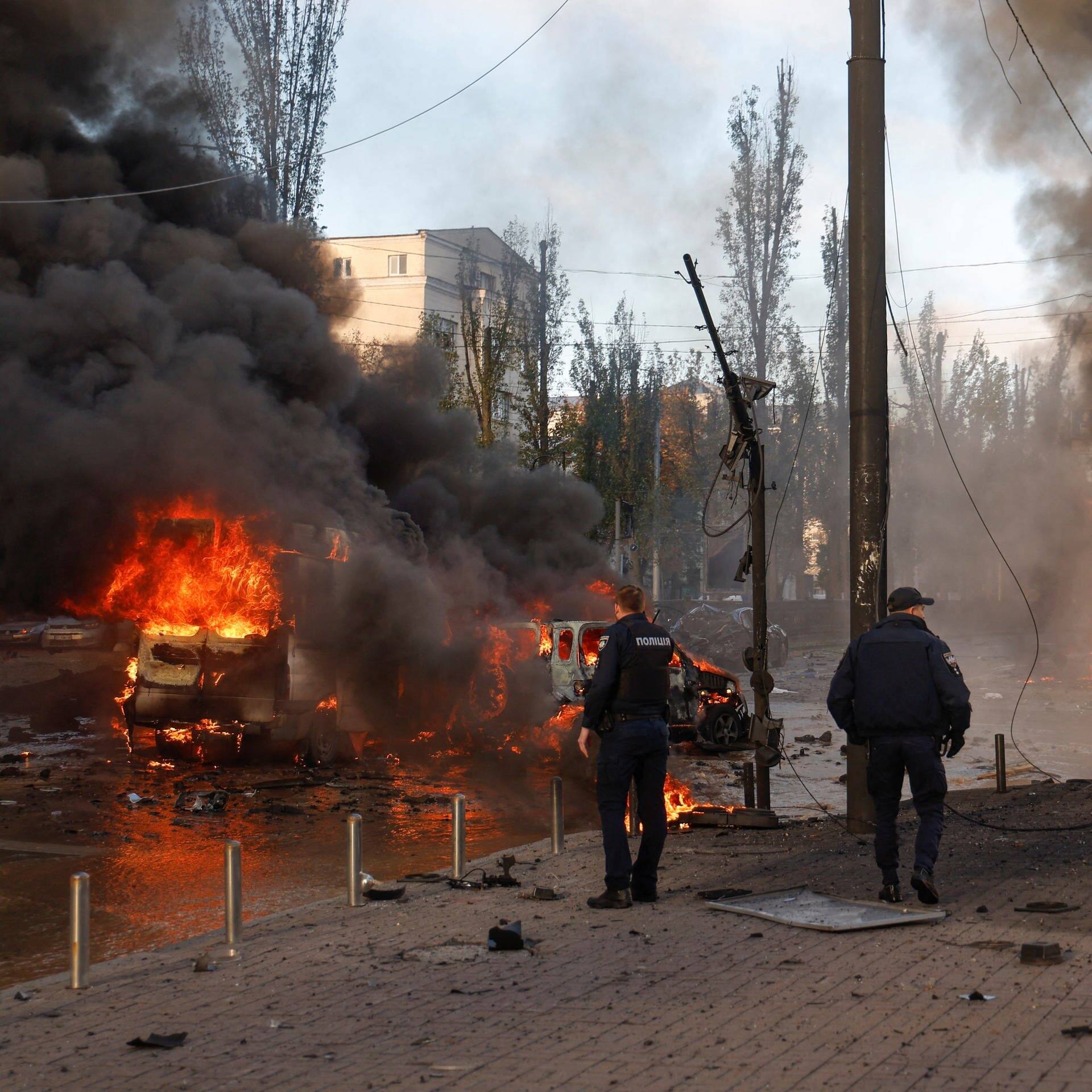 Zwei Polizisten stehen an einer Kreuzung in Kiew, auf der Autos brennen. (Foto: Reuters, REUTERS/Valentyn Ogirenko)