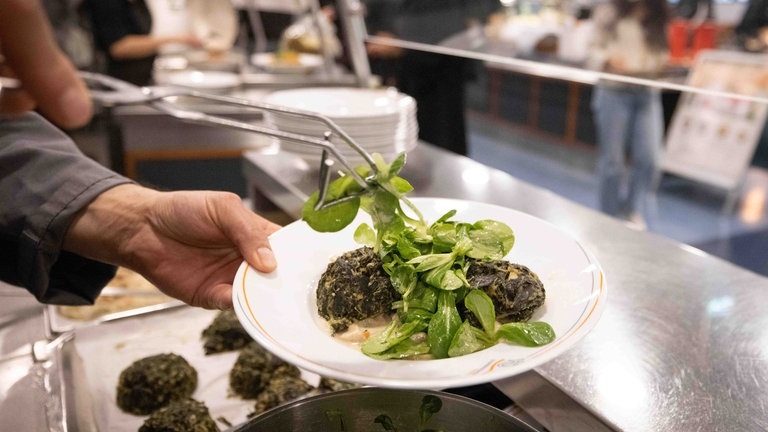 Ein Mitarbeiter bereitet einen Teller „Spinatknödel auf Pilzragout mit Feldsalat“ in der neuen Mensa der Universität Hamburg vor. (Foto: dpa Bildfunk, picture alliance/dpa | Christian Charisius)
