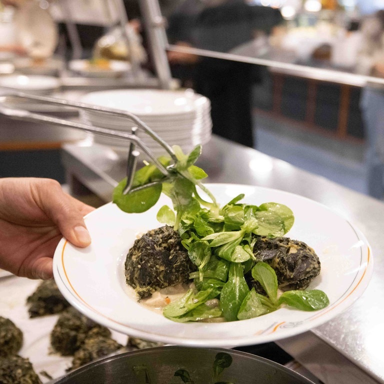 Ein Mitarbeiter bereitet einen Teller „Spinatknödel auf Pilzragout mit Feldsalat“ in der neuen Mensa der Universität Hamburg vor. (Foto: dpa Bildfunk, picture alliance/dpa | Christian Charisius)