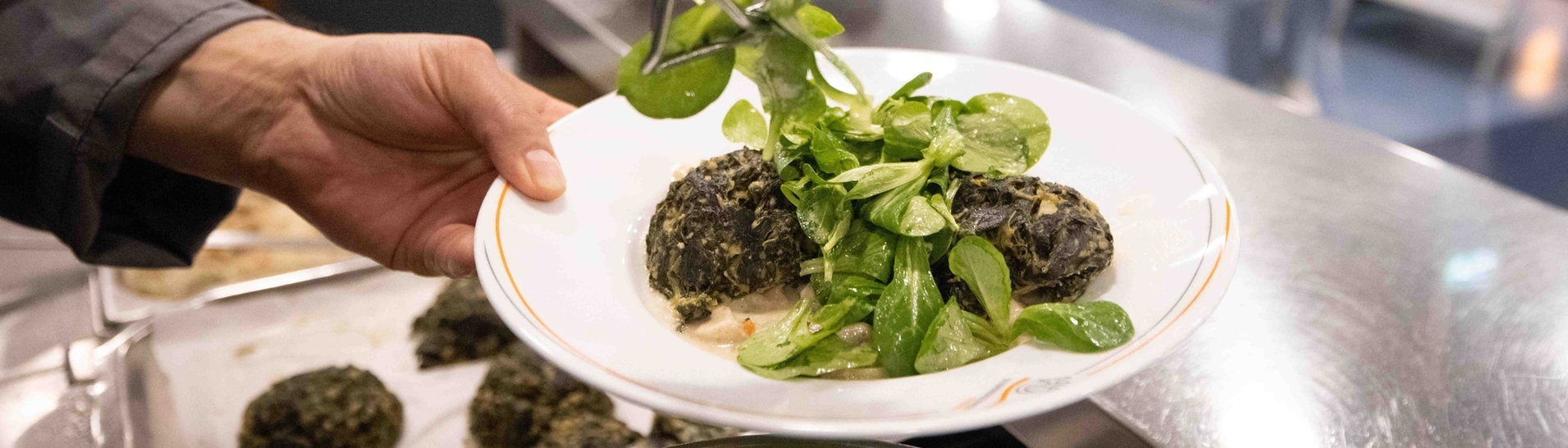 Ein Mitarbeiter bereitet einen Teller „Spinatknödel auf Pilzragout mit Feldsalat“ in der neuen Mensa der Universität Hamburg vor. (Foto: dpa Bildfunk, picture alliance/dpa | Christian Charisius)