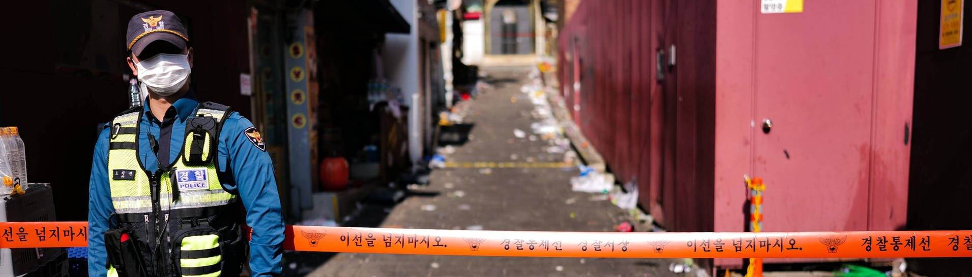 Ein Polizist steht vor einem Absperrband am Eingang zum Häuserblock in Itaewon. (Foto: IMAGO, IMAGO/NurPhoto)