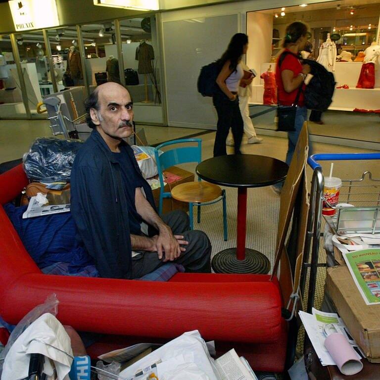Merhan Karimi Nasseri sitzt zwischen seinen Habseligkeiten im Terminal 1 des Flughafens Roissy Charles De Gaulle.  (Foto: dpa Bildfunk, picture alliance/dpa/AP | Michel Euler)