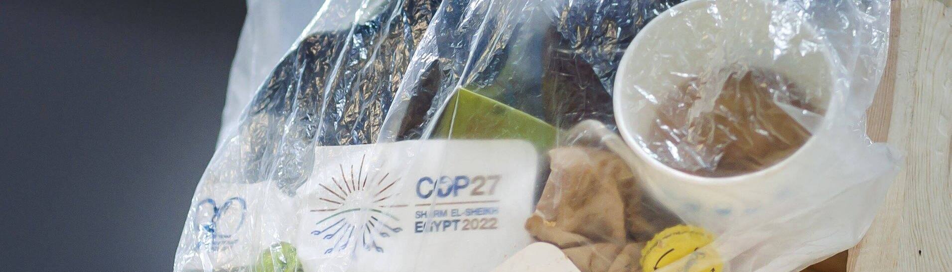 Eine Mulltüte, in der, neben einem leeren Kaffeebecher und anderem Müll, Anstecker der Weltklimakonferenz in Scharm el Scheich stecken.  (Foto: IMAGO, Imago/ Thomas Trutschel)
