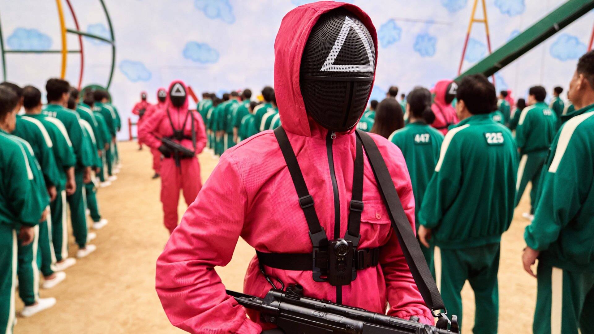 Eine Szene aus der Netflixx-Serie Squid Game. Teilnehmer der Spiele stehen, mit grünen Anzügen bekleidet, in einer Reihe und werden von bewaffneten Personen in roten Anzügen bewacht.  (Foto: IMAGO, Netflix)
