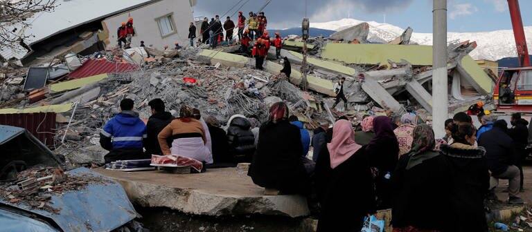 Menschen sitzen vor einem eingestürzten Gebäude in Gaziantep. (Foto: Reuters)