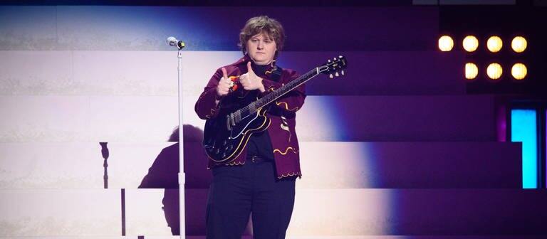 Der Sänger Lewis Capaldi steht mit einer Gitarre auf der Bühne bei den Brit Awards 2023.  (Foto: IMAGO, IMAGO / PA Images)