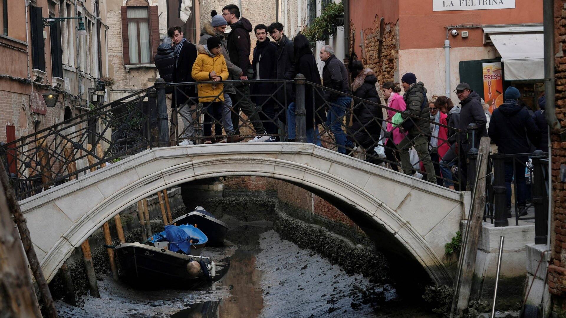 Menschen stehen auf einer Brücke in Venedig und schauen in einen Kanal, in dem sehr wenig Wasser ist (Foto: Reuters, REUTERS MAK)