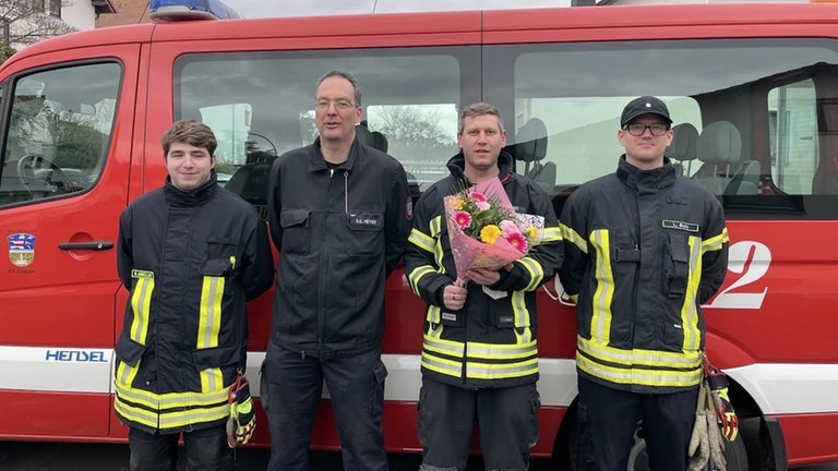 Foto: Feuerwehr Bad Nauheim Vier Feuerwehrmänner vor einem Einsatzfahrzeug mit Blumen in der Hand. (Foto: Feuerwehr Bad Nauheim)