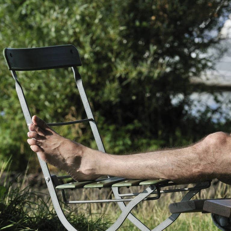Ein Mann hat seine nackten Beine auf einem Stuhl abgelegt (Foto: IMAGO, imago stock&people)