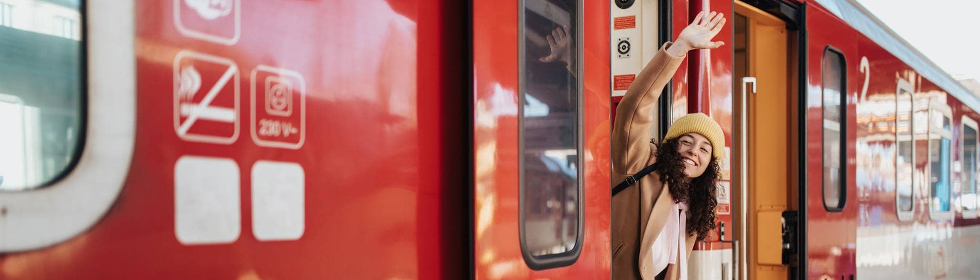 Das 49-Euro-Ticket startet jetzt. Symbolbild: Eine Frau winkt an der Tür eines Zug stehend mit grünem Koffer in der Hand (Foto: Adobe Stock, Halfpoint | Adobe Stock)