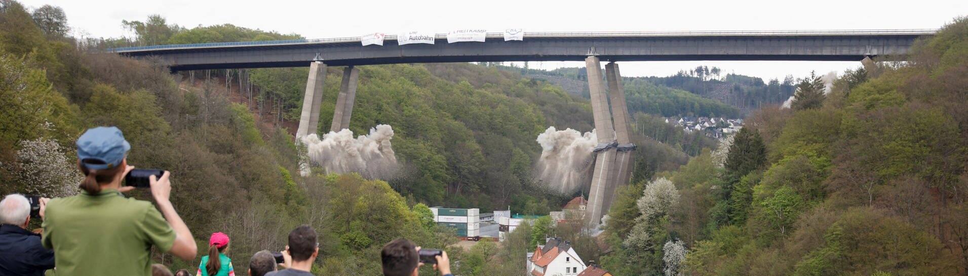 Menschen schauen aus der Ferne zu, wie die marode Rahmedetalbrücke bei Lüdenscheid gesprengt wird (Foto: Reuters, REUTERS/Leon Kuegeler)