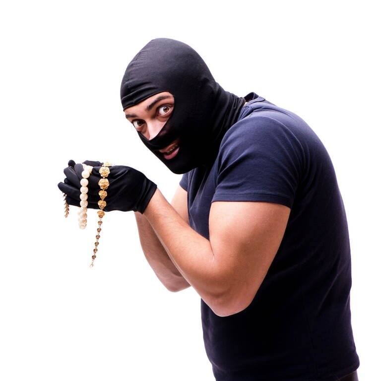 Ein mutmaßlicher Dieb mit Sturmmaske hat Goldschmuck und Goldkettenn in der Hand (Foto: IMAGO, IMAGO / agefotostock)