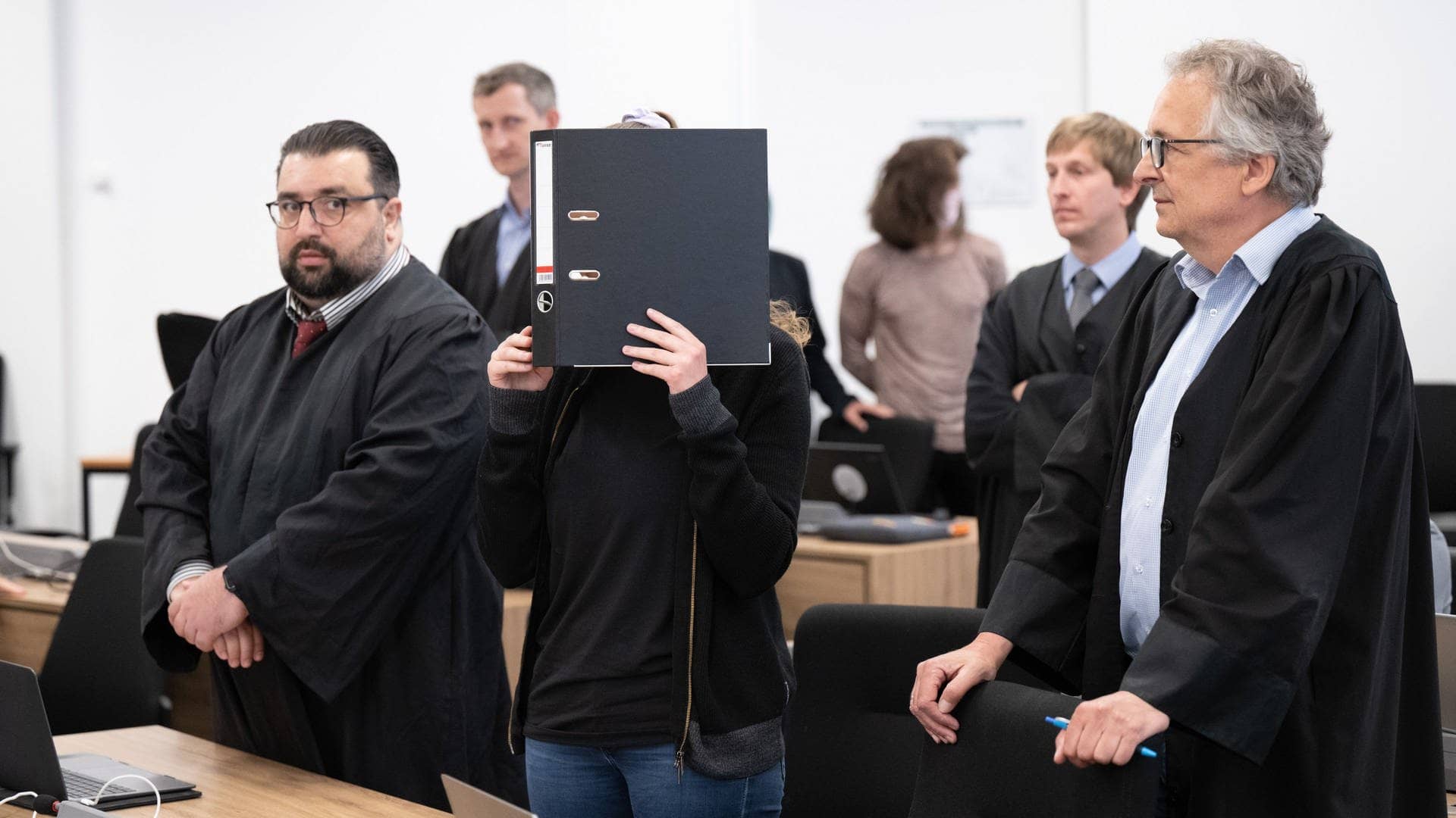 Die Angeklagte Studentin Lina E. steht neben ihren Anwälten im Gerichtssaal in Dresden und hält sich einen Ordner vors Gesicht (Foto: dpa Bildfunk, picture alliance/dpa | Sebastian Kahnert)