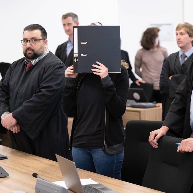 Die Angeklagte Studentin Lina E. steht neben ihren Anwälten im Gerichtssaal in Dresden und hält sich einen Ordner vors Gesicht (Foto: dpa Bildfunk, picture alliance/dpa | Sebastian Kahnert)