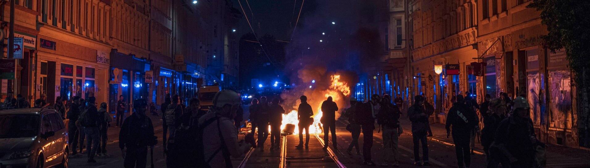 Eine Reihe von Polizisten steht vor einer brennenden Barrikade in Leipzig-Connewitz (Foto: IMAGO, IMAGO/Moritz Schlenk)