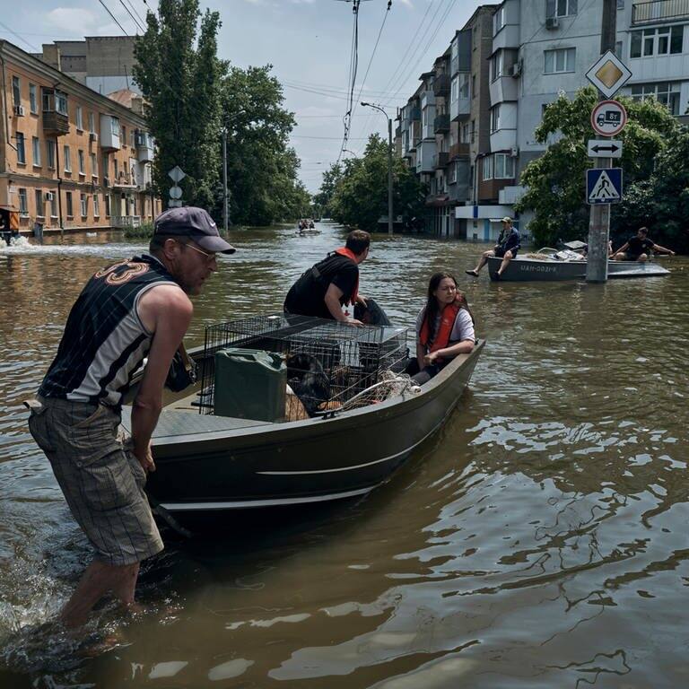 Menschen mit Haustieren werden mit einem Boot aus einem überfluteten Stadtteil evakuiert. In den Fluten sind mindestens 14 Menschen gestorben.