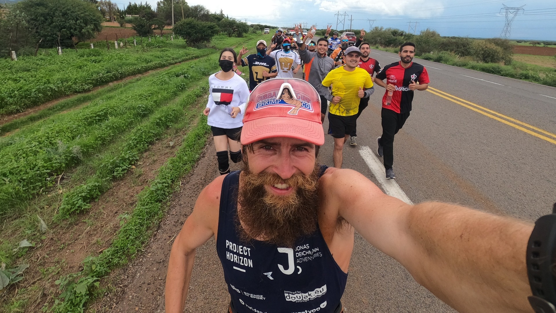 Jonas Deichmann, deutscher Extremsportler, fotografiert sich während seines Triathlons um die Welt selbst. Im Hintergrund Anhänger, die mit ihm ein Stück laufen.  (Foto: dpa Bildfunk, picture alliance/dpa/Jonas Deichmann | Jonas Deichmann)