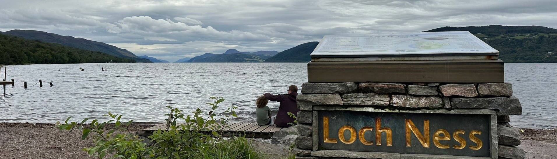 Menschen sitzen am Ufer des Loch Ness in Schottland. (Foto: dpa Bildfunk, picture alliance/dpa | Benedikt von Imhoff)