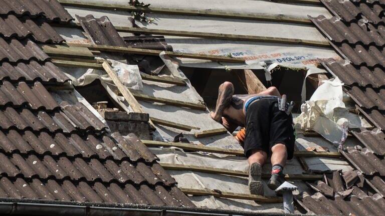 Dachdeckermeisterin verteidigt Azubi gegenüber Kundin. Auf dem Bild ist zu sehen: Ein Mitarbeiter eines Dachdeckerunternehmens schaut in ein großes Loch in einerm Dach. (Symbolbild) (Foto: dpa Bildfunk, picture alliance/dpa | Bernd Thissen)