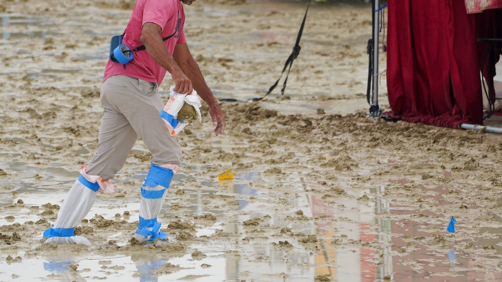 Ein Mann hat sich Plastiktüten um die Schuhe gebunden und läuft durch den Matsch beim Burning Man (Foto: IMAGO, IMAGO/USA TODAY Network)