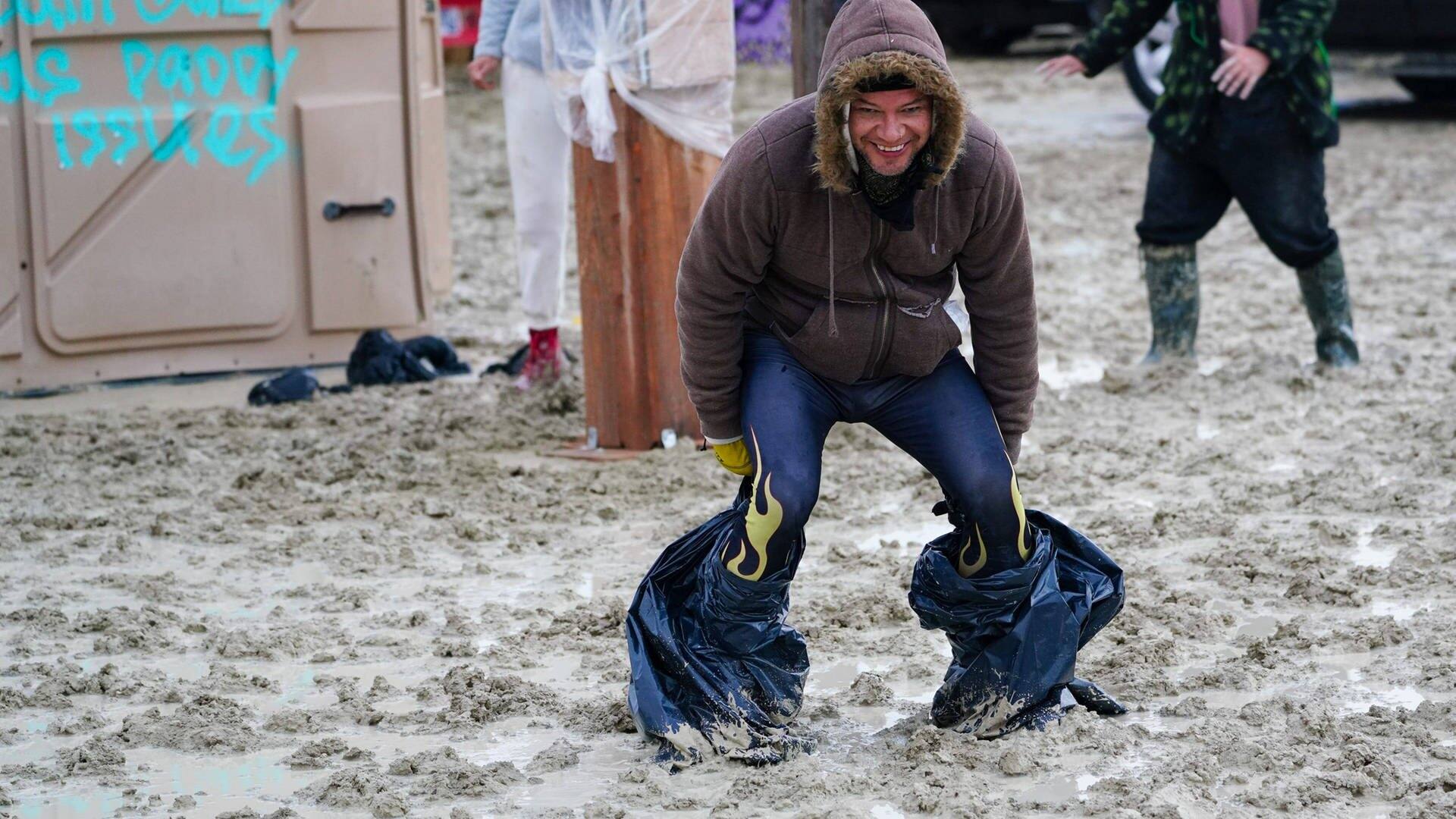 Ein Festivalbesucher steht mit Plastiktüten an den Füßen im Matsch und lacht (Foto: IMAGO, IMAGO/USA TODAY Network)