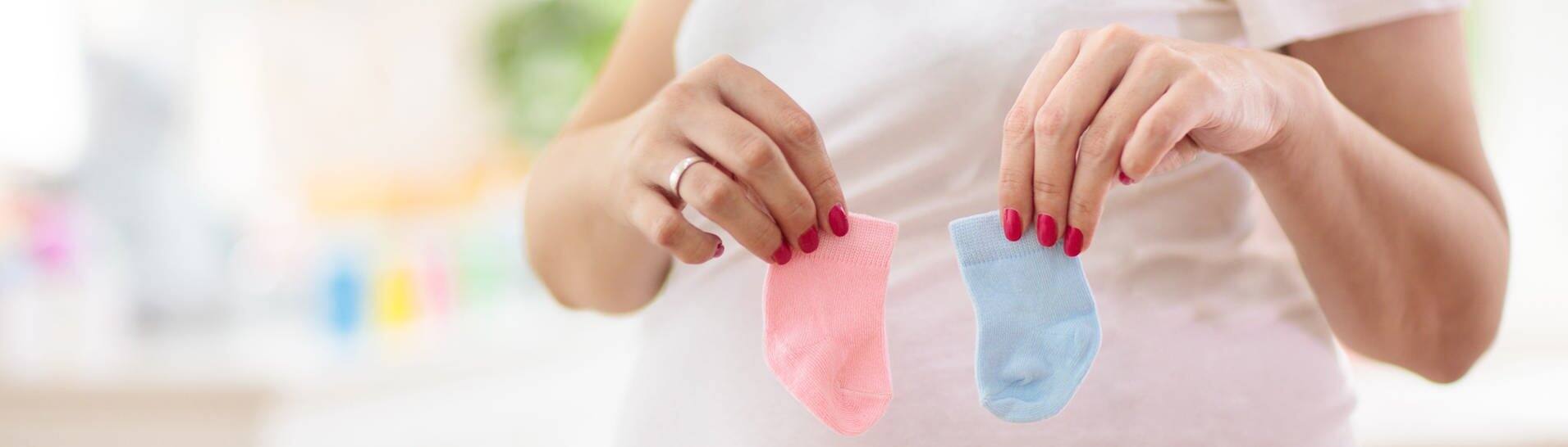 Gender Reveal: Schwangere Frau hält rosa und blaue Söckchen in der Hand (Foto: IMAGO, IMAGO / Pond5 Images)