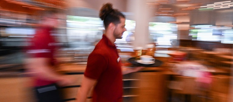 Eine Bedienung in einem Restaurant trägt ein Tablett mit Getränken. (Foto: dpa Bildfunk, picture alliance/dpa | Bernd Weißbrod)