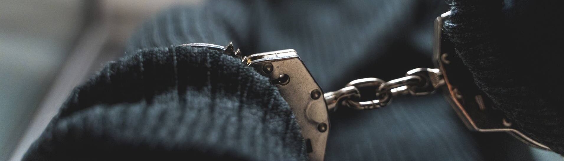 Ein Einbrecher in Handschellen (Symbolbild) - Mutmaßlicher Räuber in New York wegen seiner bunten Unterhose überführt (Foto: IMAGO, IMAGO / Bihlmayerfotografie)