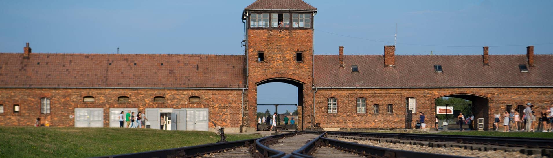 Besucher gehen vor dem historischen Tor (Innenseite) durch das frühere Vernichtungsslager Auschwitz-Birkenau. Die Gedenkstätte kann jetzt mit einer Online-Live-Führung besucht werden. (Foto: dpa Bildfunk, picture alliance/dpa | Monika Skolimowska)