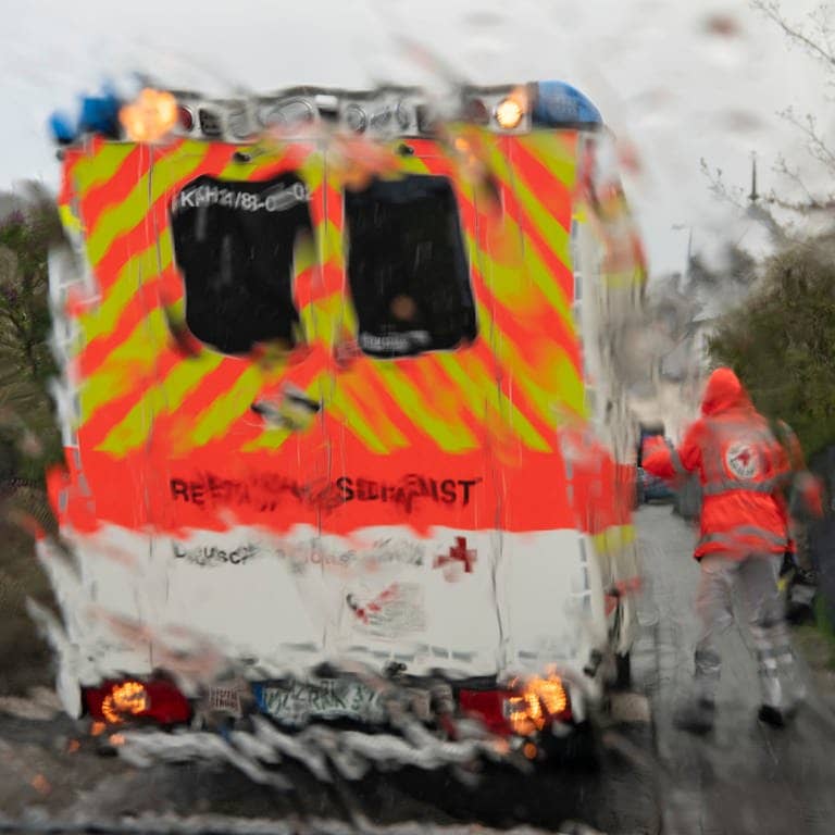 (Symbolbild) Im strömenden Regen geht ein Notfallsanitäter des Deutschen Roten Kreuzes (DRK) zu einem Rettungswagen, der vor dem Haus eines Patienten steht.  (Foto: dpa Bildfunk, picture alliance/dpa | Boris Roessler)