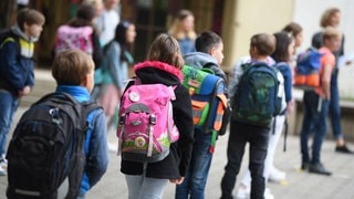 Schülerinnen und Schüler einer Grundschule stehen mit Abstand zueinander auf dem Schulhof