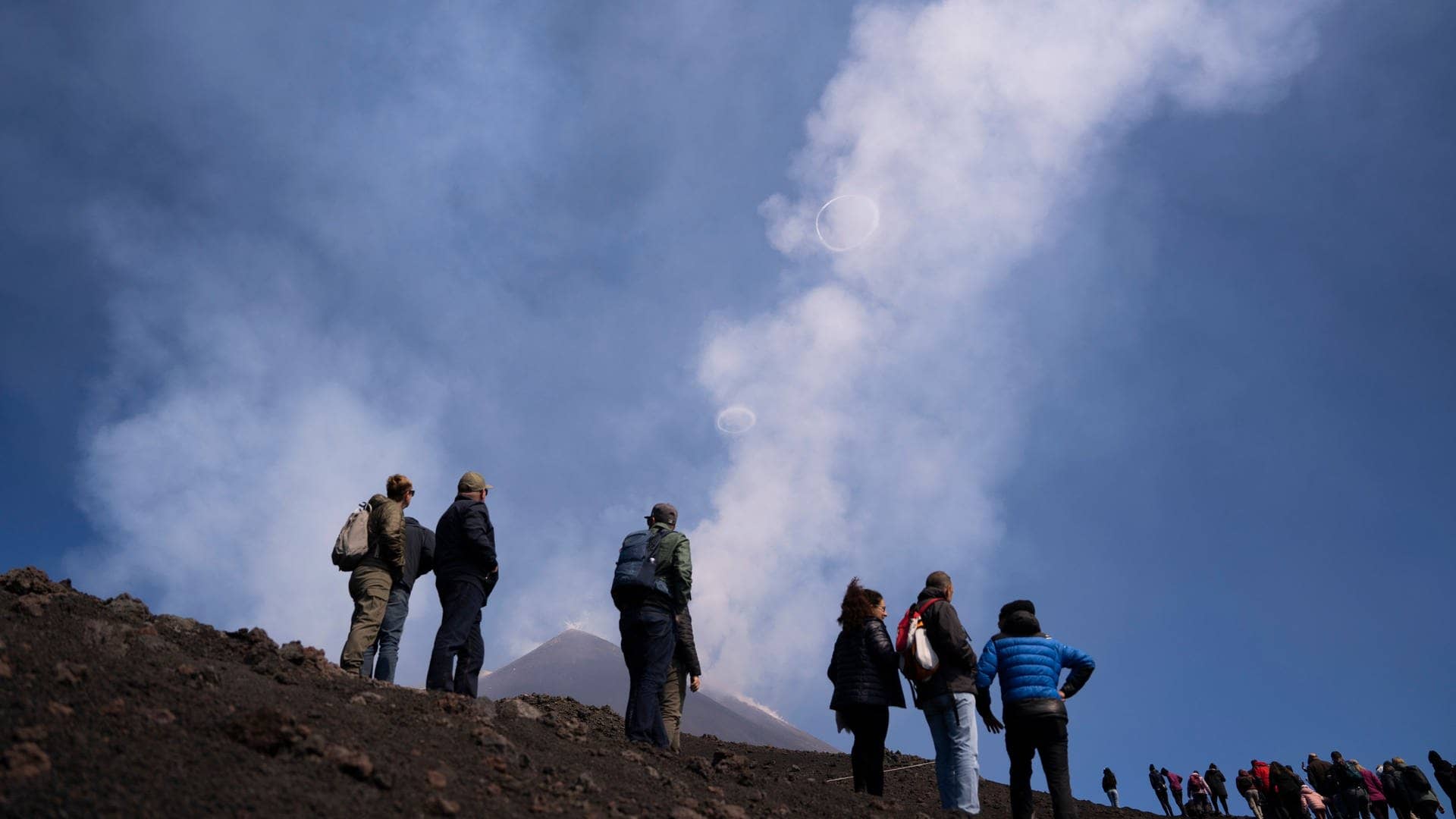 Menschen schauen zu, wie der Vulkan Ätna in Sizilien Ringe aus Rauch in den Himmel spuckt. (Foto: dpa Bildfunk, picture alliance/dpa/AP/dpa | Giuseppe Di Stefano)