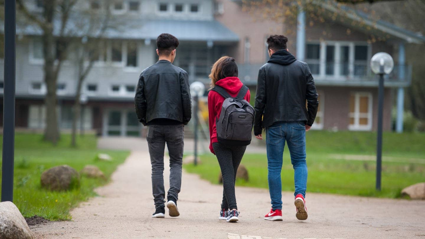 Drei Jugendliche gehen über das Gelände einer Schule.
