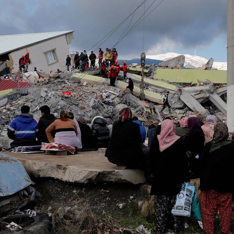 Menschen sitzen vor einem eingestürzten Gebäude in Gaziantep.