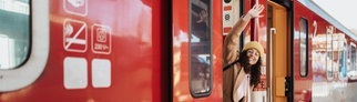 Das 49-Euro-Ticket startet jetzt. Symbolbild: Eine Frau winkt an der Tür eines Zug stehend mit grünem Koffer in der Hand