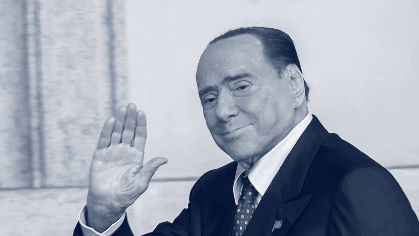 Silvio Berlusconi winkt in die Kamera, das Bild ist schwarz-weiß.