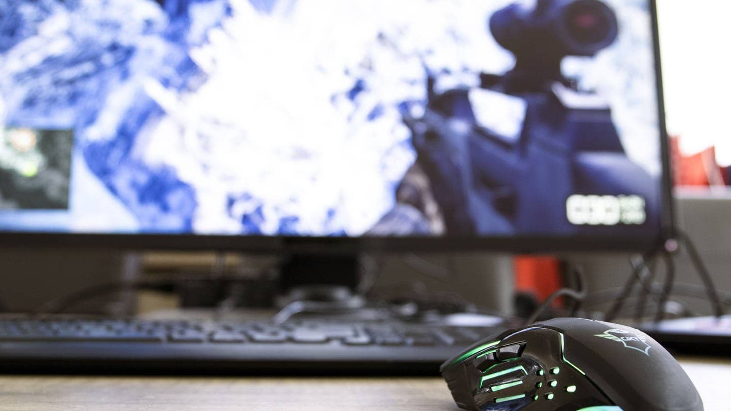Eine Gaming-Maus vor einem Bildschirm, auf dem ein Ego-Shooter läuft (Foto: IMAGO, IMAGO / Pond5)