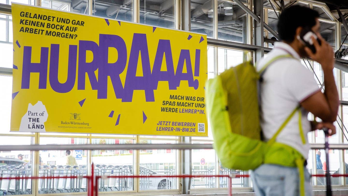 Ein umstrittenes Plakat des Kultusministzeriums hängt am Flughafen Stuttgart