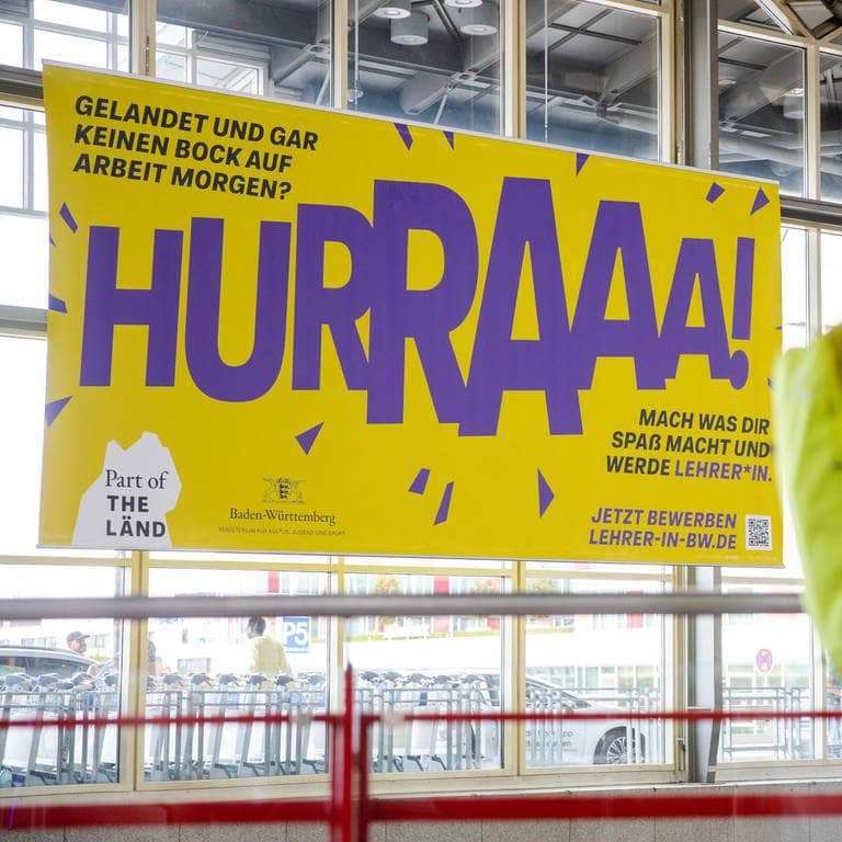Ein umstrittenes Plakat des Kultusministzeriums hängt am Flughafen Stuttgart