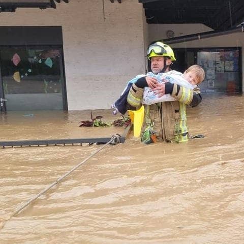 Feuerwehrmann Sandi Zajc trägt ein Kind aus einem überfluteten Kindergarten